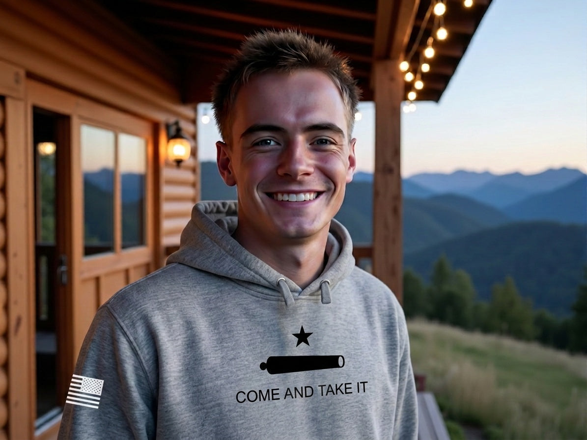 Man wearing Gun Beaver Come and Take It hoodie on a rustic cabin porch at dusk